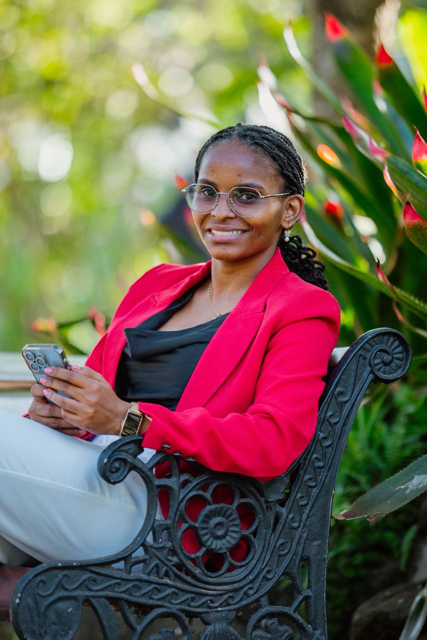 Jackline Ngowi seated outdoors in a red blazer.
