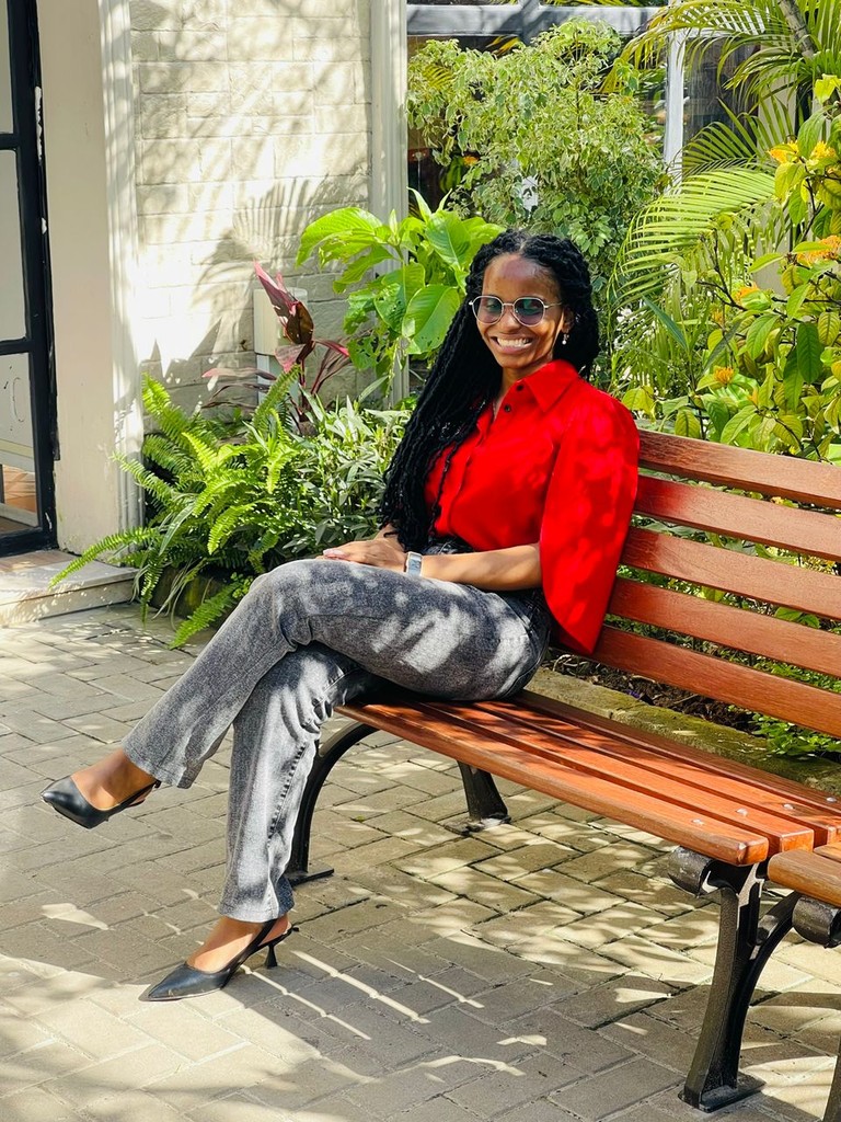 Jackline Ngowi seated on a bench in a red top.