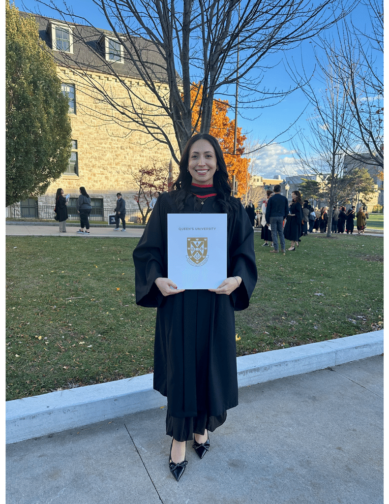 Rachel Di Iorio in academic regalia holding a Queen's University folder outdoors.