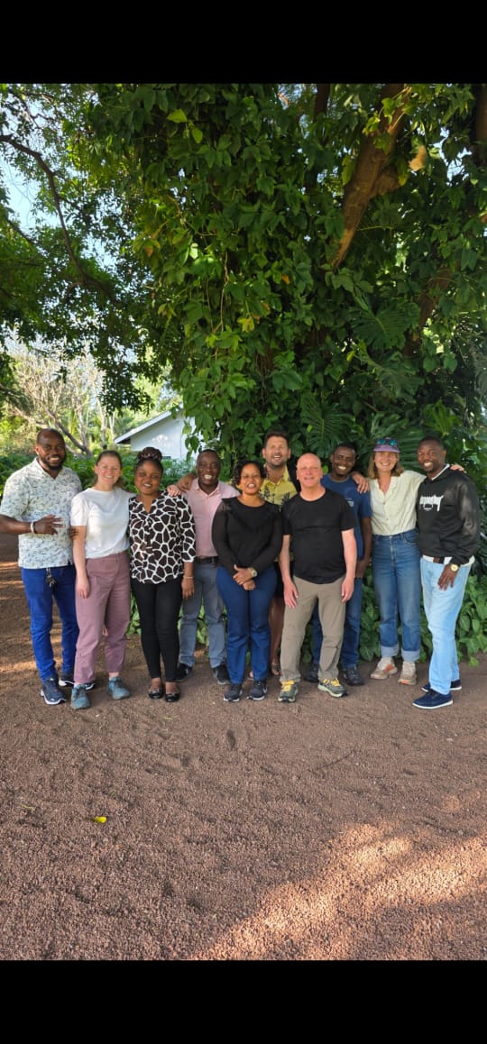 A group of unnamed people standing together beneath a tree outdoors.