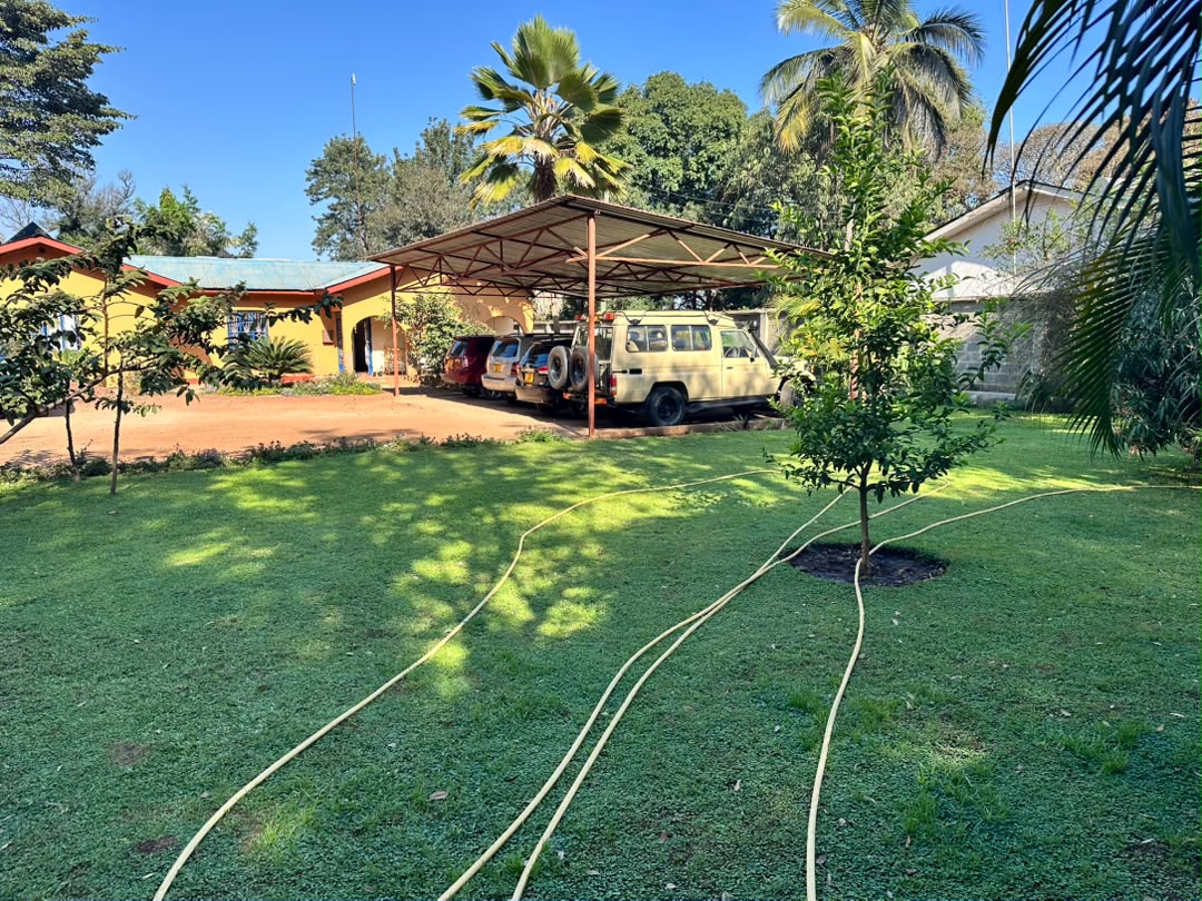 A lawn with garden hoses, trees, covered parking and vehicles on the WHIT grounds.
