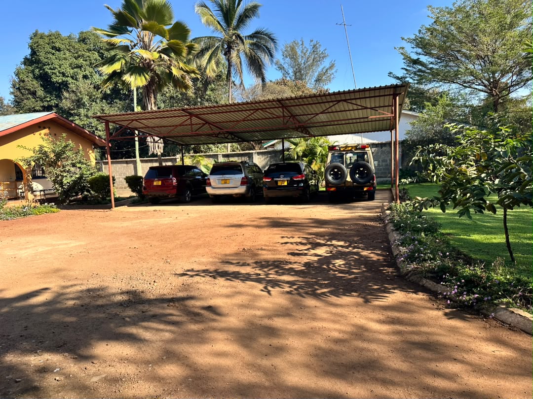 Covered vehicle parking between yellow buildings, trees and garden areas.